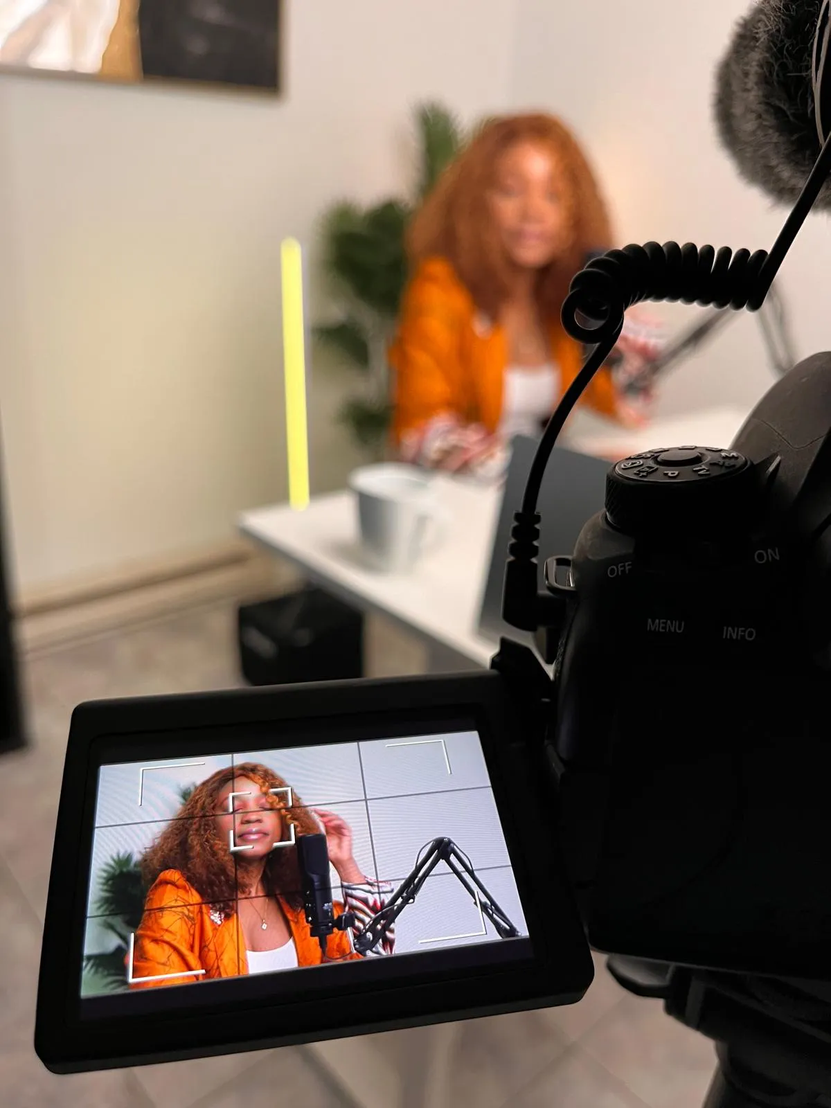 Camera screen framing a podcast host at her microphone